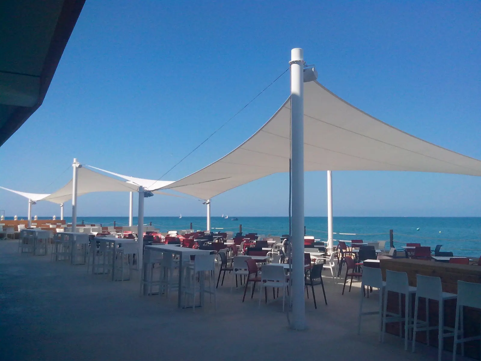 Vela tensada blanca sobre una terraza junto a la playa