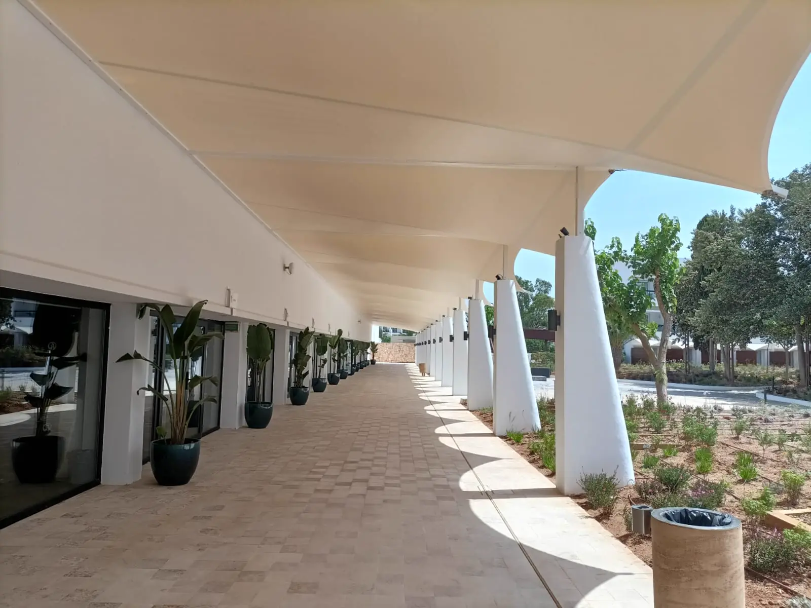 Pasillo exterior cubierto por una membrana textil sobre pilares blancos