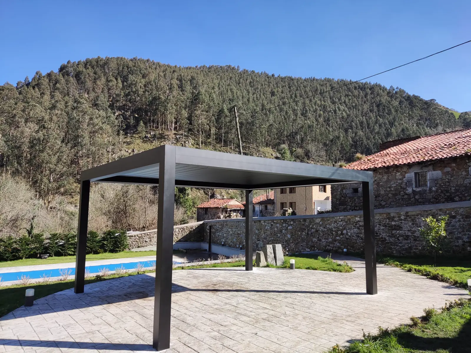 Pérgola bioclimática gris en un jardín con piscina y montaña