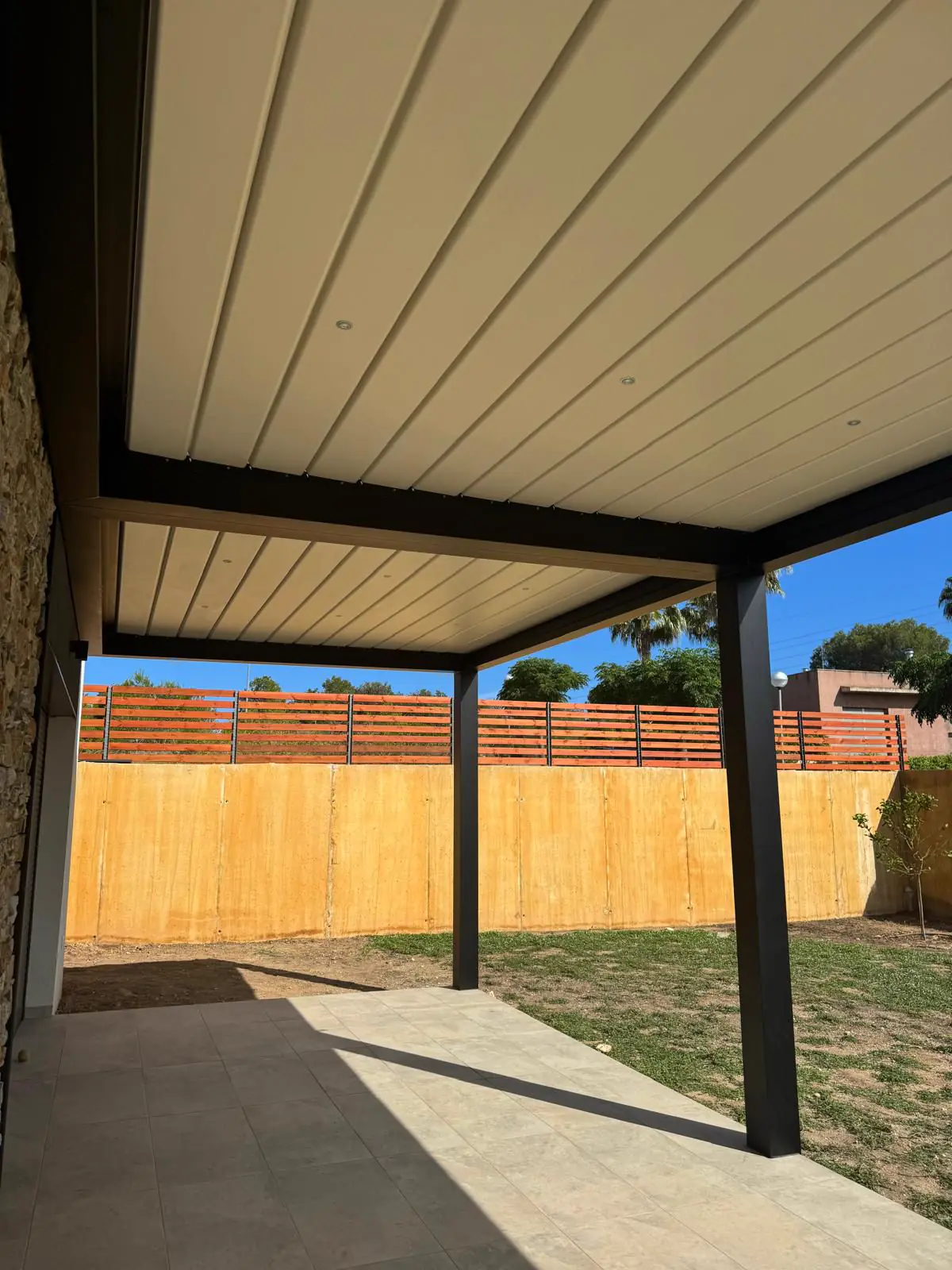 Pérgola bioclimática blanca junto a una valla de madera