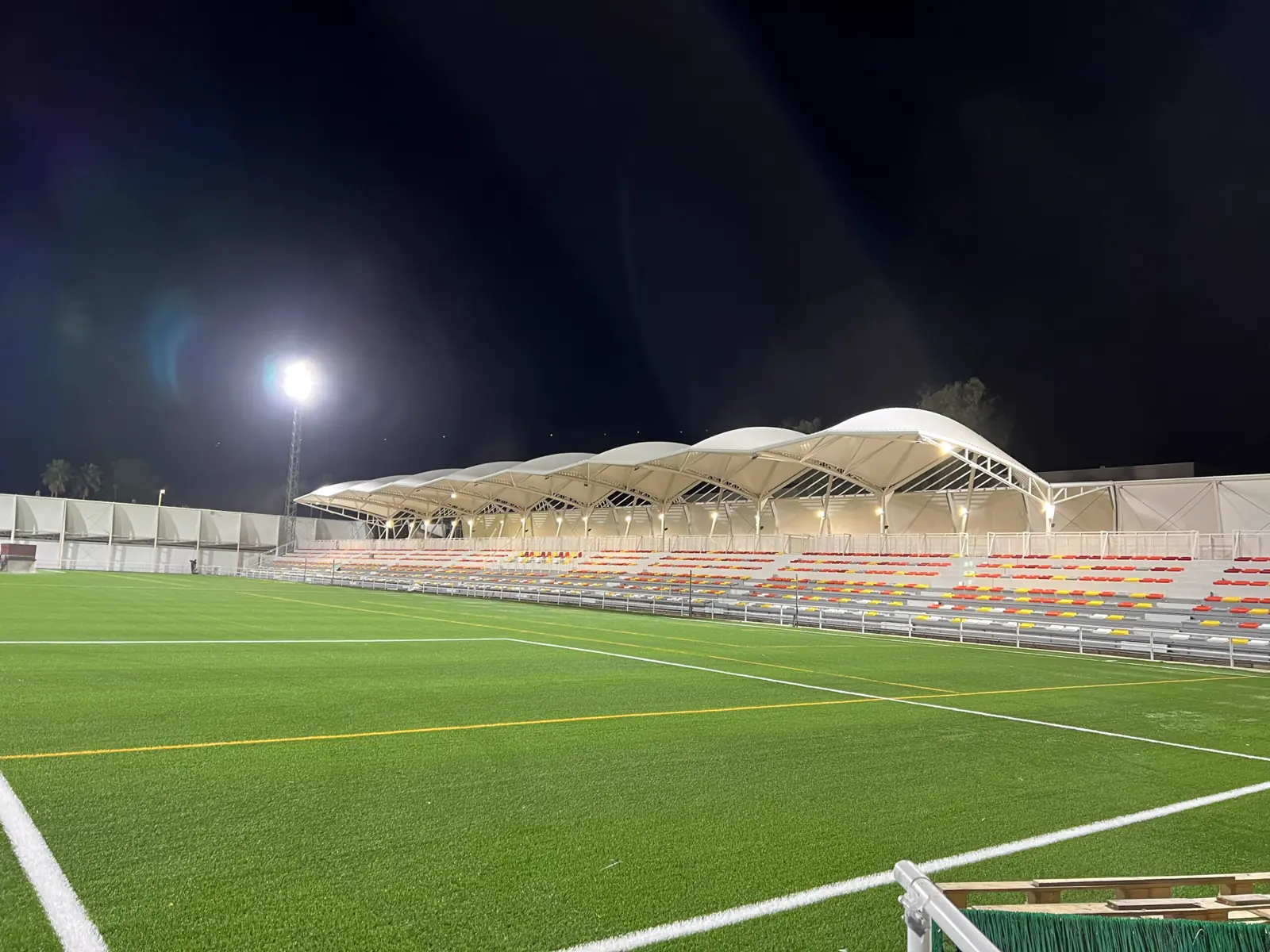 Campo de fútbol de noche con la cubierta textil de la grada iluminada